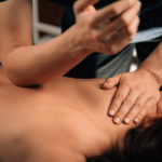 Massage therapist applying deep tissue massage techniques to patient's upper back.